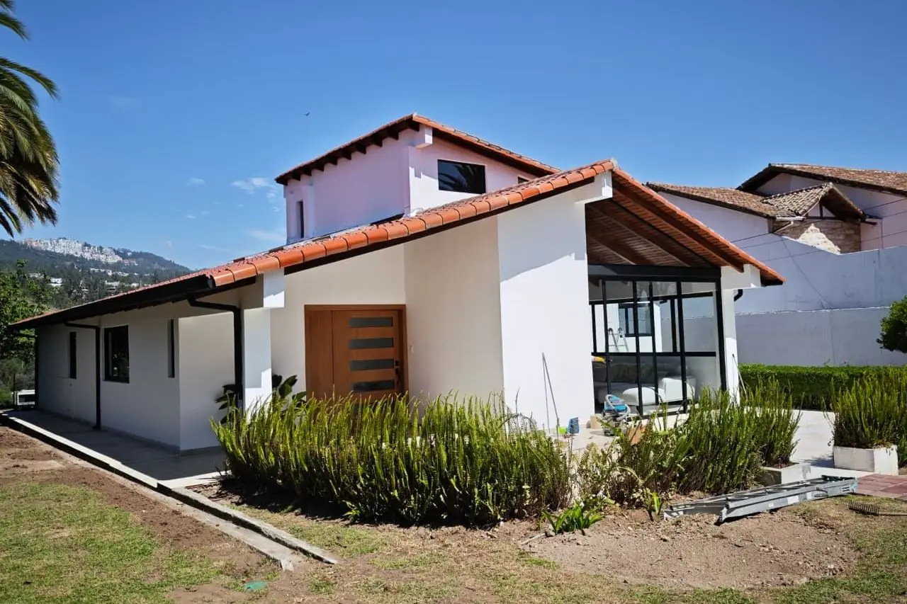 Fachada de la casa remodelada en Cumbayá con techo de teja, puerta de madera y ventanales negros