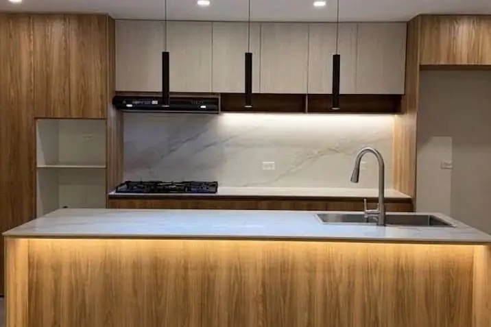 Cocina abierta con isla iluminada, muebles de madera y lámparas colgantes