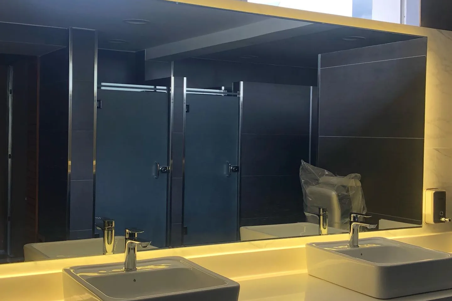Baño del Club de Tenis Buena Vista con cabinas de vidrio, mesón iluminado y lavabos