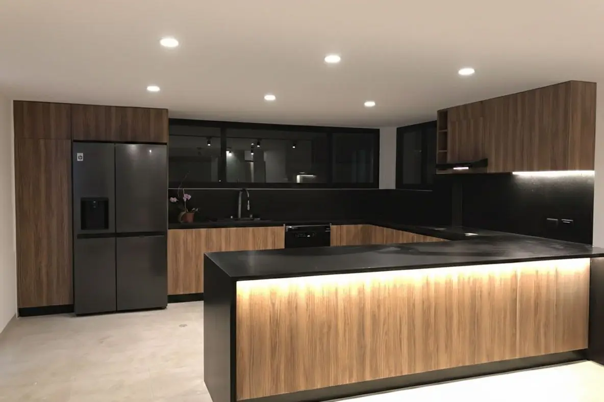 Cocina terminada con muebles de madera, mesones de granito negro e iluminación LED