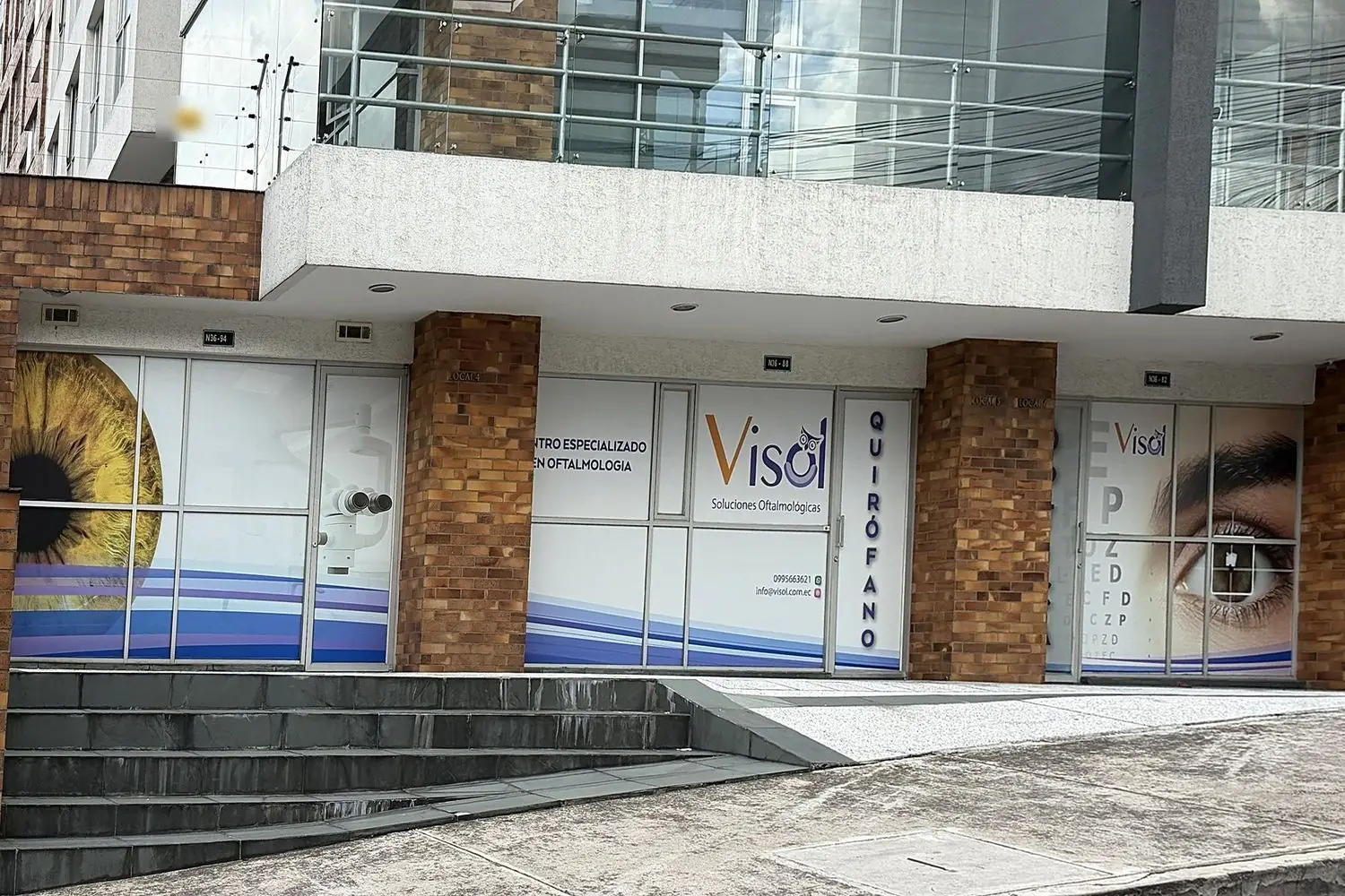 Fachada del consultorio oftalmológico con quirófano: los dos locales comerciales unidos, con vitrinas rotuladas y acceso con rampa