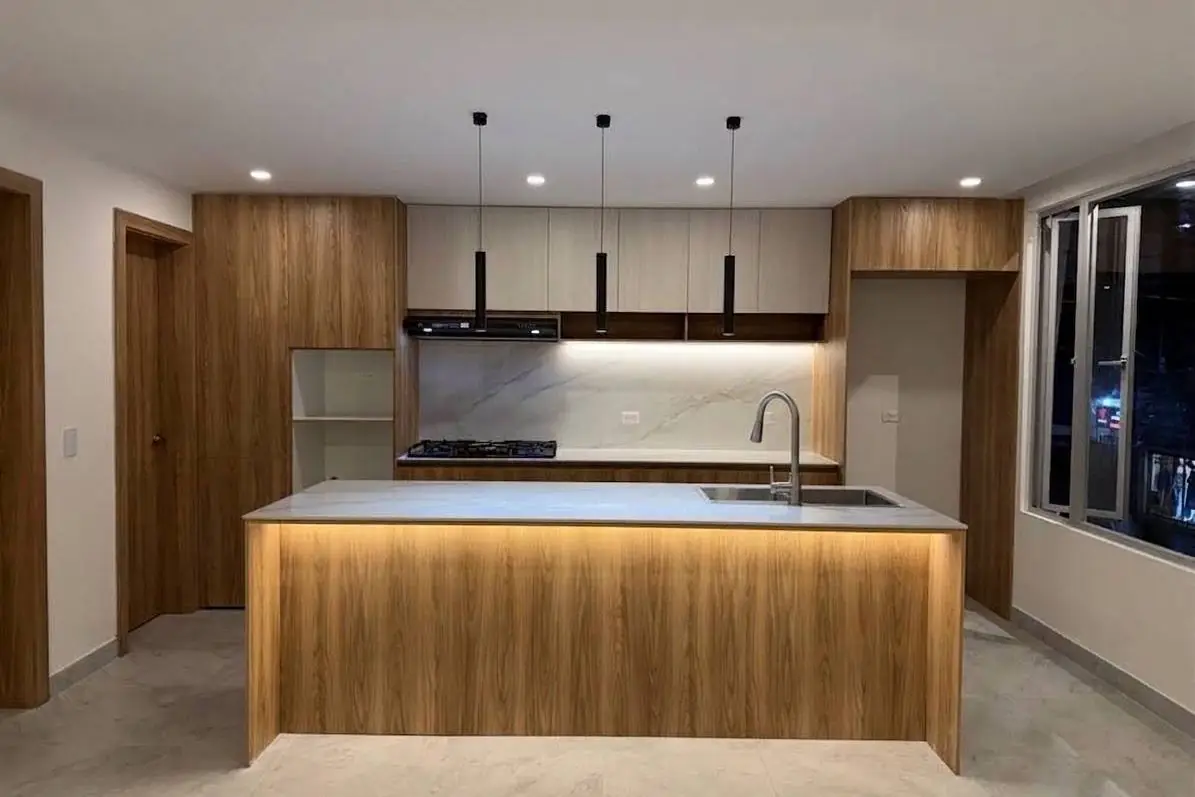 Cocina terminada con isla iluminada, muebles de madera y lámparas colgantes