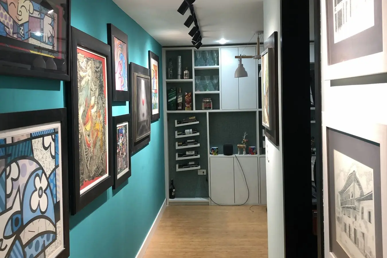 Pasillo remodelado en Monteserrín, con pared turquesa, cuadros de la familia e iluminación en riel