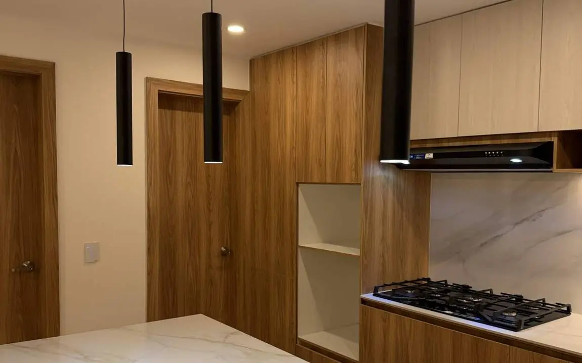 Cocina remodelada por HOA Arquitectura en San Carlos, Quito: isla con mesón tipo mármol, muebles de madera y lámparas colgantes