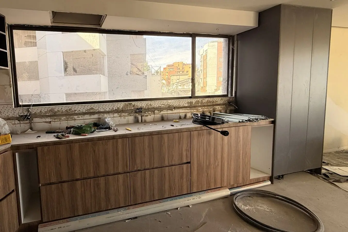 Cocina del dúplex en Quito Tennis en obra: muebles bajos en madera, torres grises y ventanal con vista a la ciudad