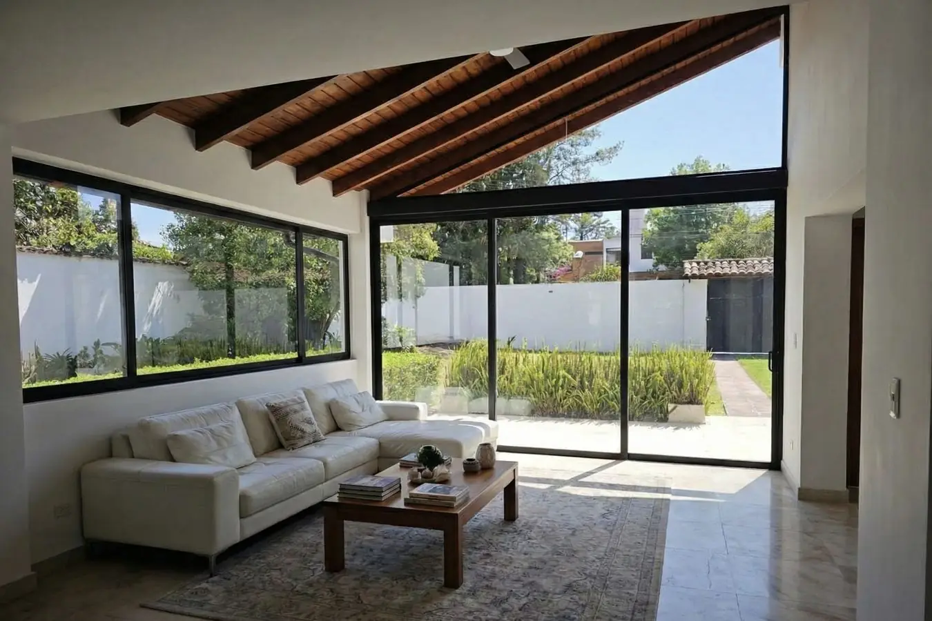 Sala de la casa remodelada en Cumbayá con techo de vigas de madera y ventanales de piso a techo hacia el jardín
