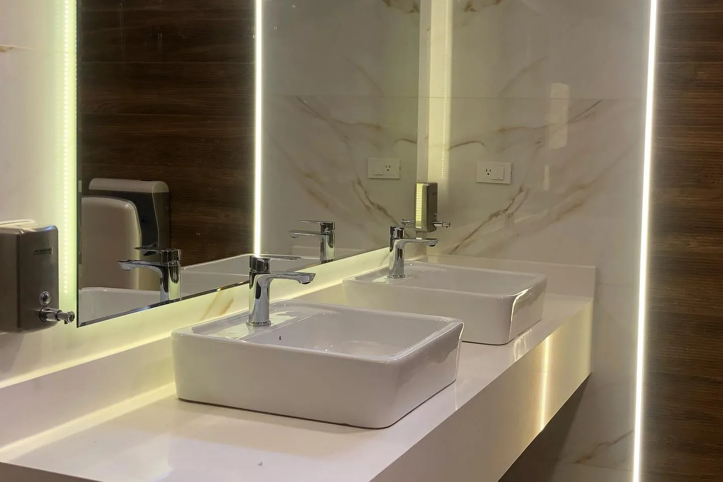 Baño remodelado del Club de Tenis Buena Vista con mesón blanco, lavabos de sobreponer, espejo con iluminación LED y revestimiento de madera