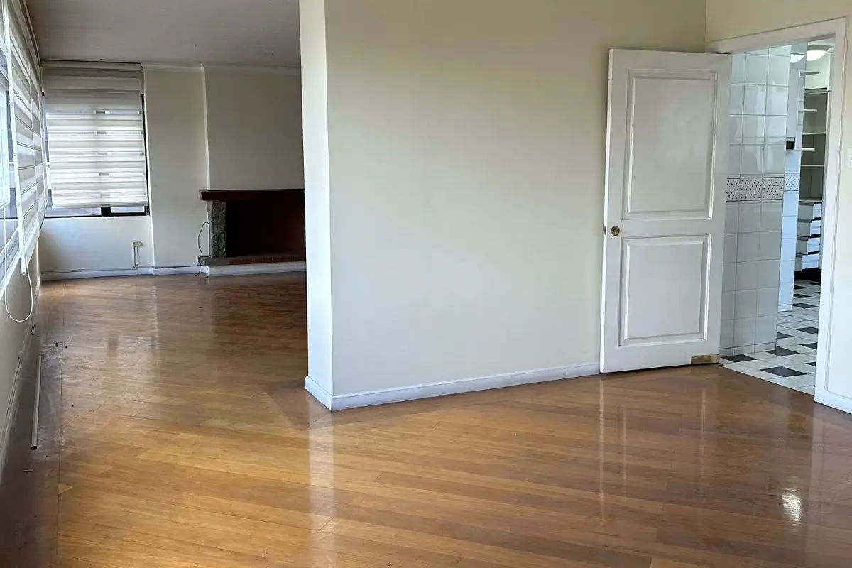 Sala del dúplex en Quito Tennis antes de la remodelación, con piso de madera y chimenea