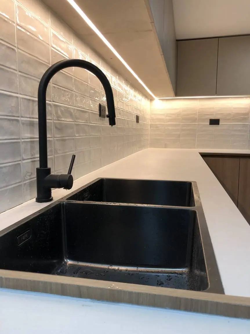 Detalle del lavaplatos y la grifería negros con luz LED bajo los muebles