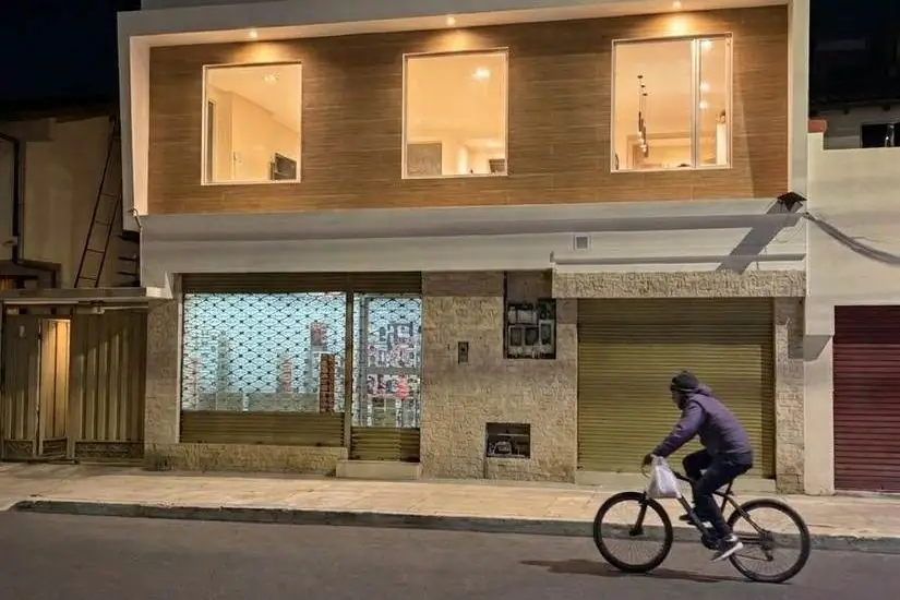 Fachada terminada de noche de la ampliación en San Carlos, Quito: nueva planta alta revestida e iluminada sobre el local comercial